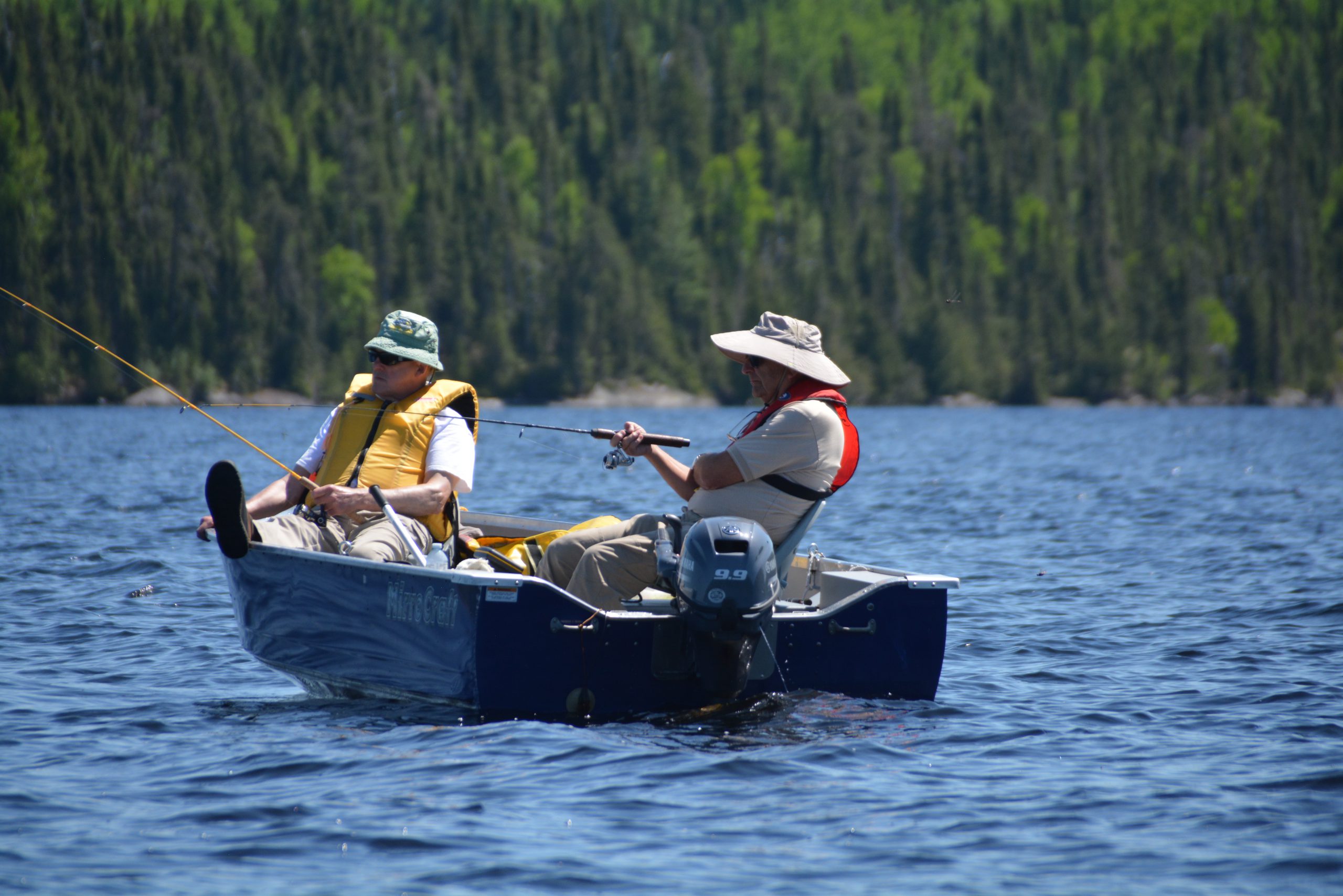 Two gentlemen out fishing in a motorboat on the lake.